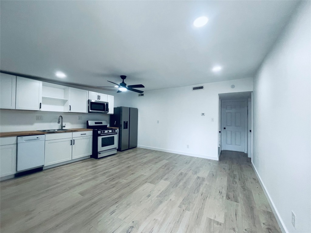 7107 Guadalupe Street, Unit 202 Austin, TX 78752 - Photo 2 of 8 Kitchen with appliances with stainless steel finishes, white cabinets, open shelves, light wood-style floors, and a ceiling fan