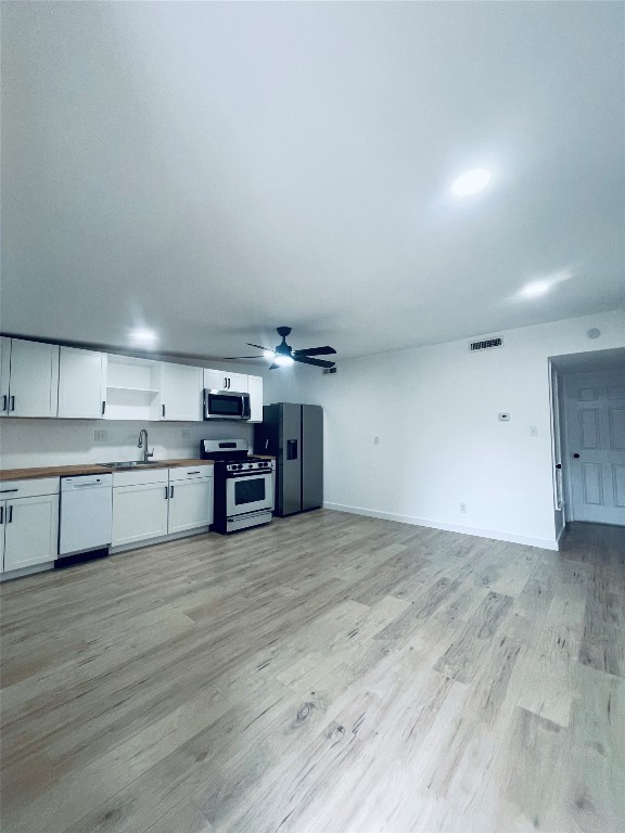 7107 Guadalupe Street, Unit 202 Austin, TX 78752 - Photo 3 of 8 Kitchen featuring white cabinetry, stainless steel appliances, light wood-type flooring, a ceiling fan, and open shelves
