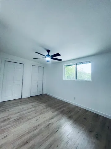 an empty room with wooden floor chandelier fan and windows