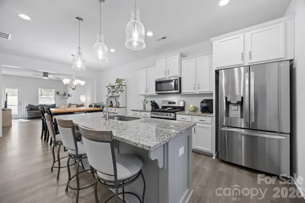 a kitchen with stainless steel appliances granite countertop a refrigerator a stove a sink a dining table and chairs with wooden floor