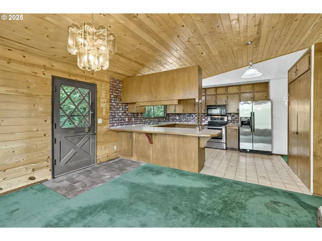 a view of a kitchen with kitchen island a large window cabinets a sink and stainless steel appliances