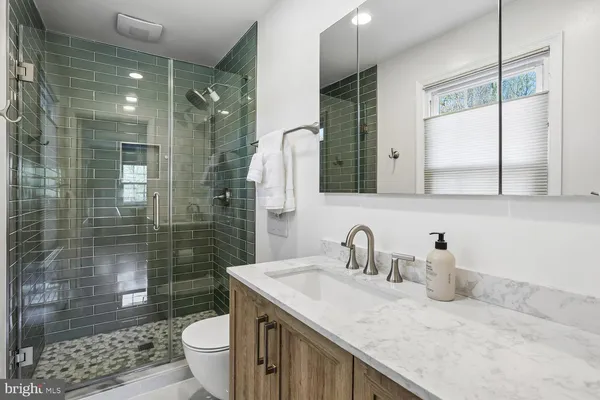 a bathroom with a granite countertop sink a toilet a mirror and shower
