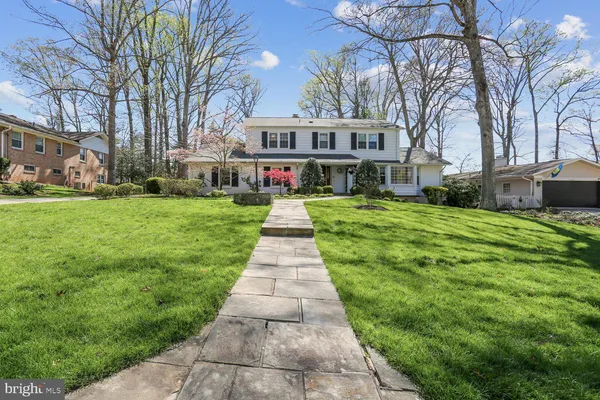 a view of a white house in front of a big yard with plants and large trees