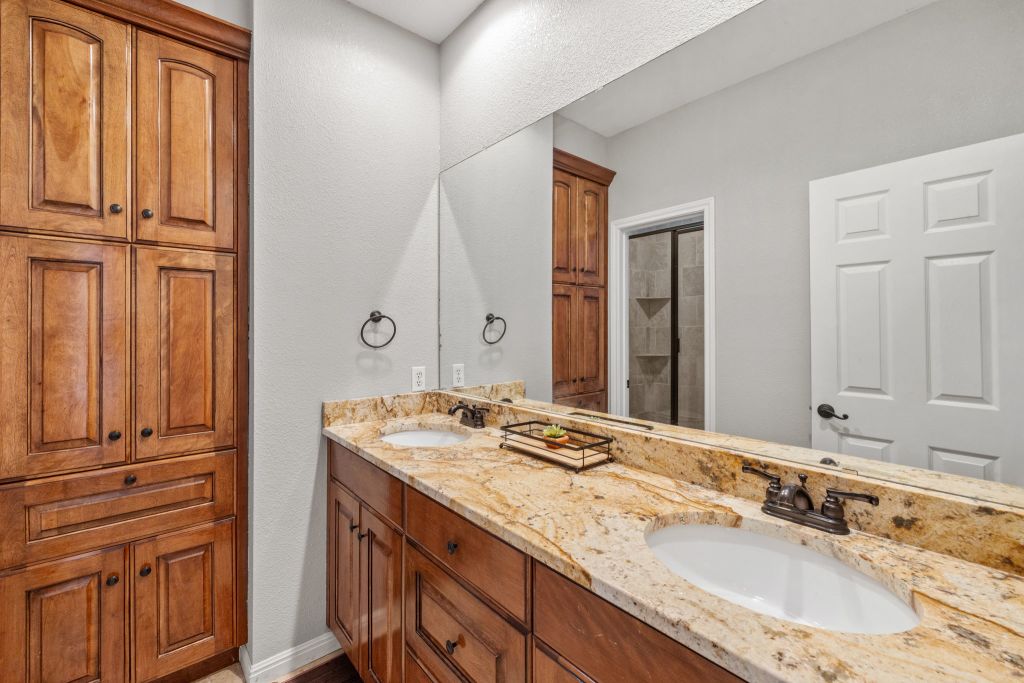 10800 Beach Road Leander, TX 78641 - Photo 15 of 39 Dual vanities with golden granite counters and rich wood cabinetry define this well-appointed bathroom.