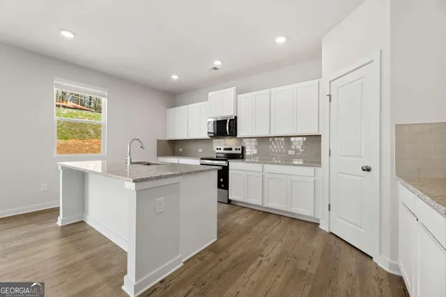 a kitchen with stainless steel appliances granite countertop a sink a stove top oven and white cabinets