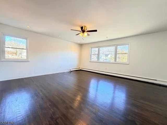 a view of an empty room with wooden floor and a ceiling fan