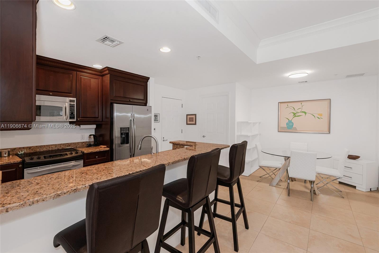 100 Andalusia Avenue, Unit 210 Coral Gables, FL 33134 - Photo 10 of 29 a kitchen with stainless steel appliances kitchen island granite countertop a table chairs and a refrigerator