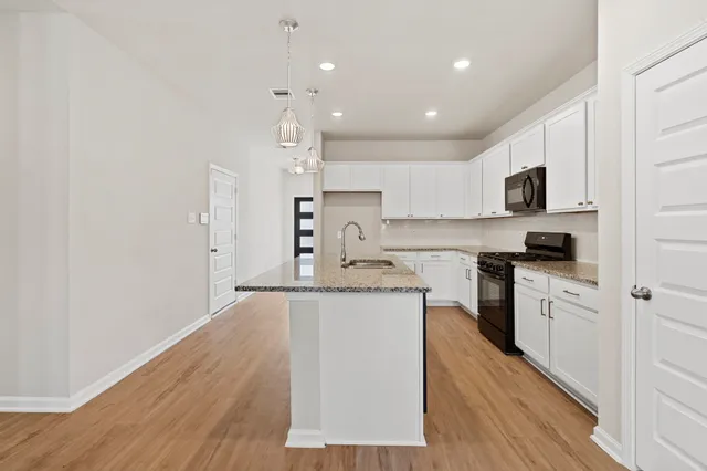 a kitchen with granite countertop a stove top oven a sink a refrigerator and white cabinets with wooden floor