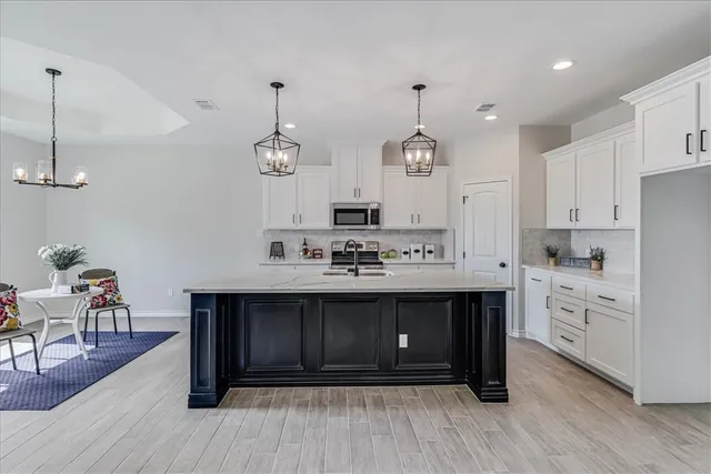 a kitchen with stainless steel appliances granite countertop a sink dishwasher a stove and white cabinets with wooden floor