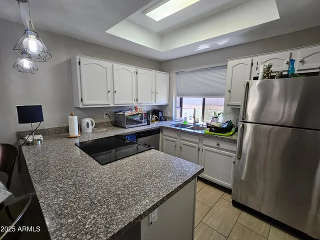 a kitchen with granite countertop a refrigerator a stove a sink dishwasher and white cabinets with wooden floor