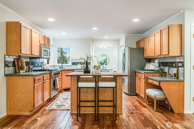 a kitchen with stainless steel appliances granite countertop a refrigerator a stove top oven a sink dishwasher and white cabinets with wooden floor
