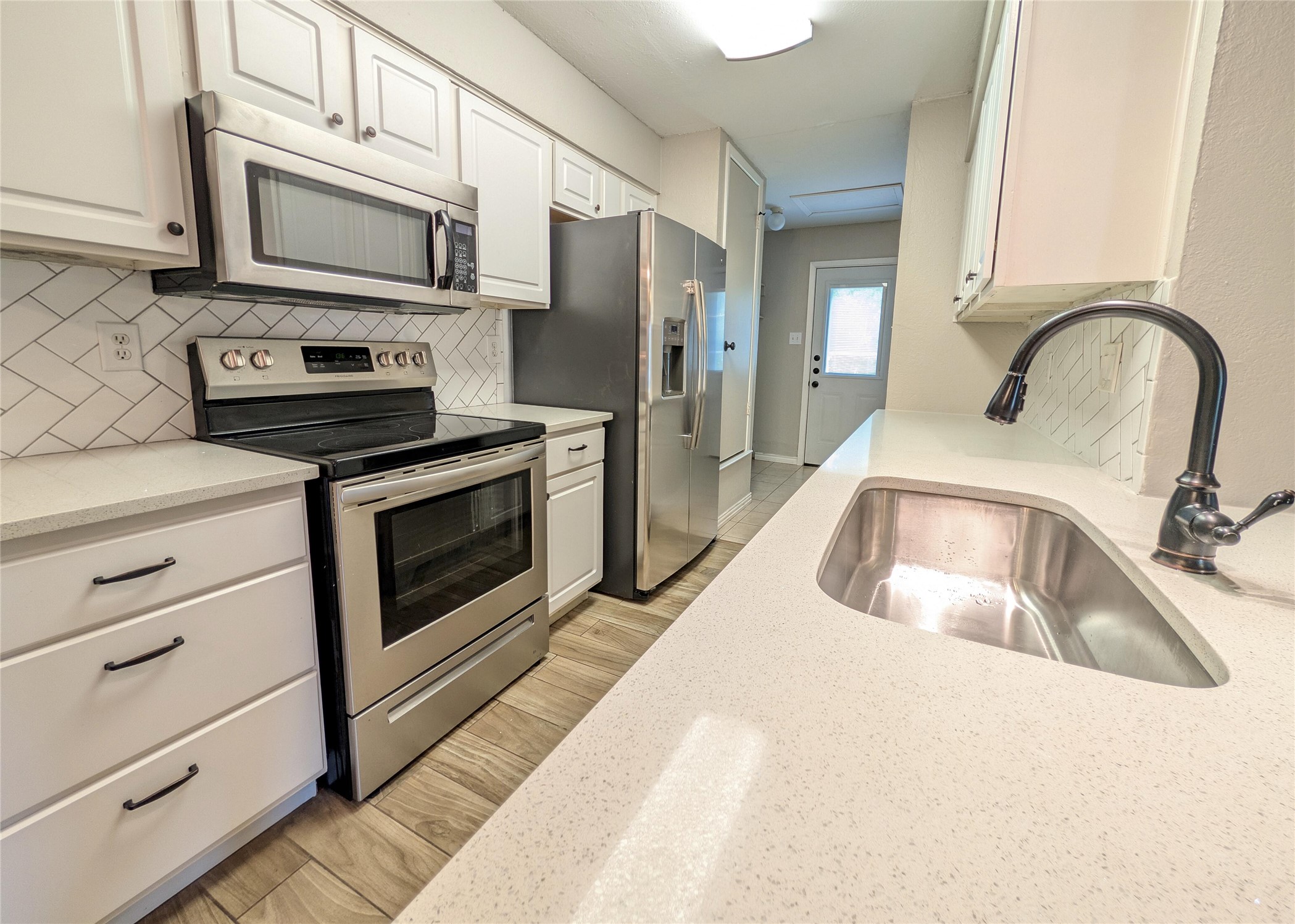 12601 Turtle Rock Road, Unit B Austin, TX 78729 - Photo 3 of 20 Stainless Steel appliances and large sink. Quartz countertops and tile backsplash and floor. Lots of cabinet space. Laundry and back door through kitchen.