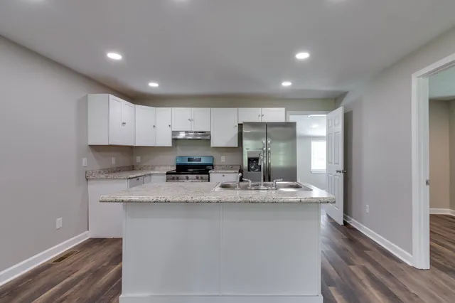 a kitchen with stainless steel appliances granite countertop a sink a stove a refrigerator cabinets and a wooden floor