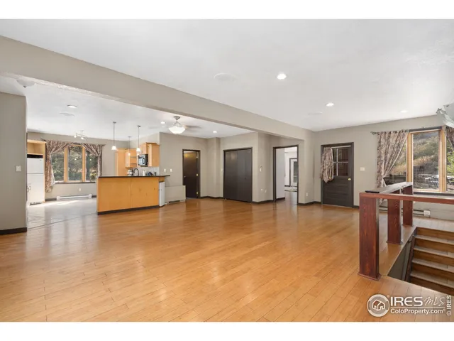 a view of an empty room with wooden floor and a kitchen