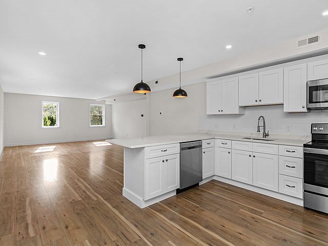 1 Pleasant Street, Unit 305 Cohasset, MA 02025 - Photo 7 of 24 a kitchen with granite countertop a stove a sink and white cabinets with wooden floor