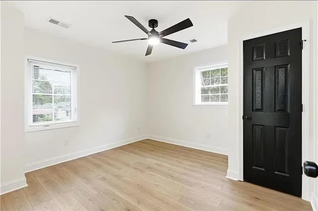 an empty room with wooden floor ceiling fan and windows