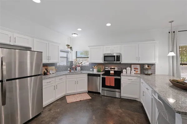 a kitchen with stainless steel appliances granite countertop white cabinets a sink a stove a microwave and a refrigerator