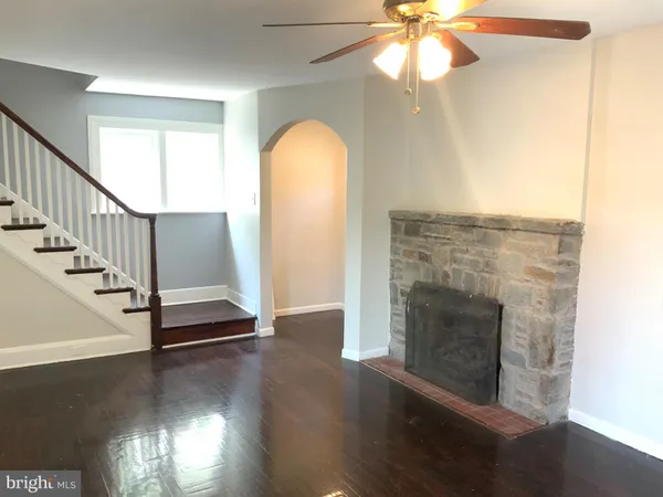 a view of a livingroom with wooden floor a fireplace a ceiling fan and a window
