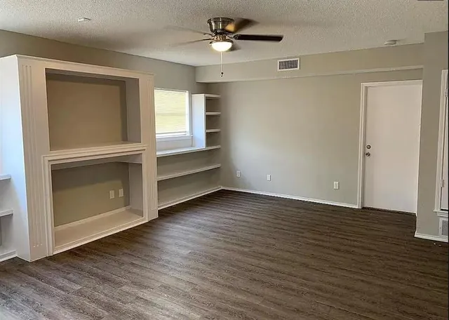 an empty room with wooden floor a ceiling fan and windows