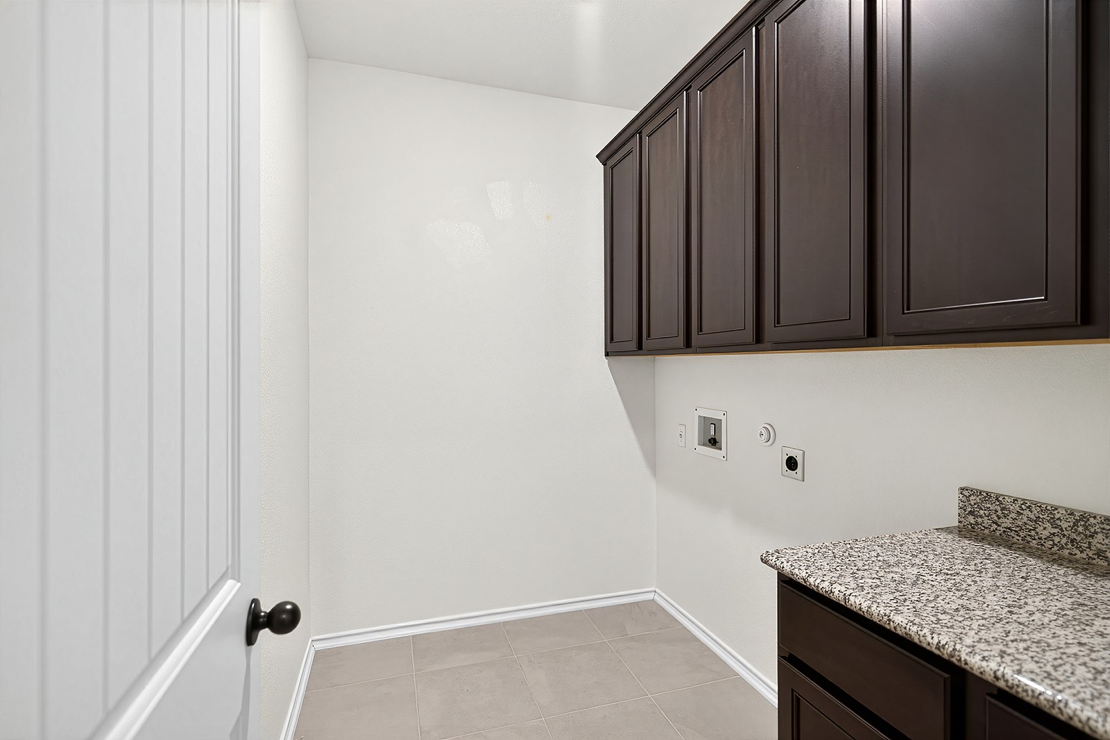 4600 Ercolano Lane Round Rock, TX 78665 - Photo 20 of 37 Dedicated utility space featuring dark wood-finish cabinetry, granite-style countertop, and neutral tile flooring