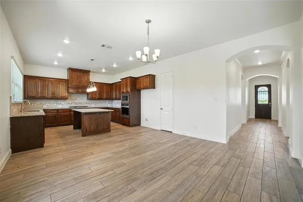 a large kitchen with stainless steel appliances granite countertop a sink dishwasher a stove and a kitchen island with wooden floor