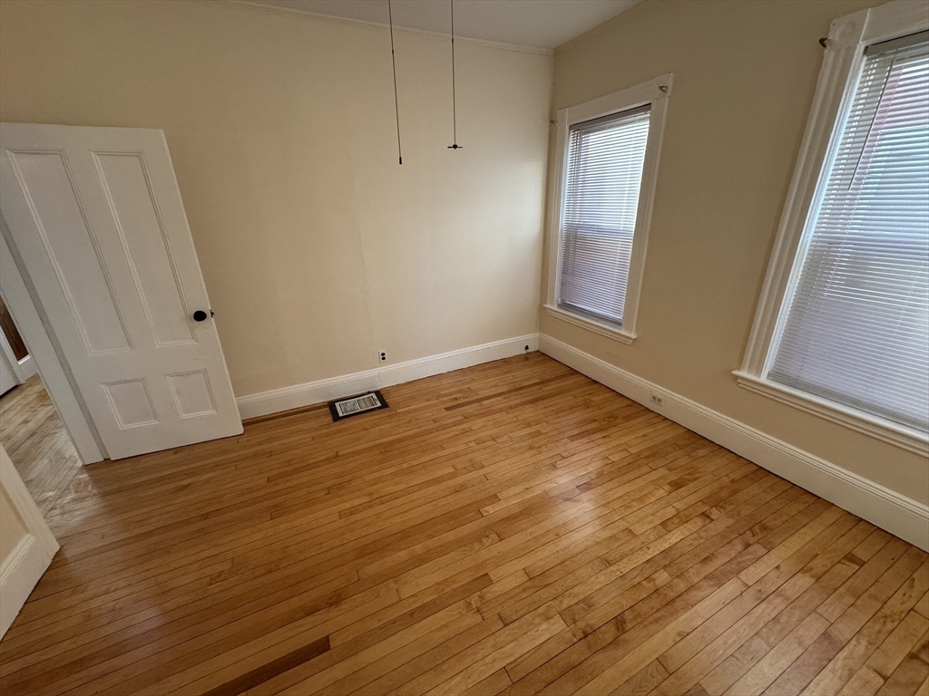 377 Highland Avenue, Unit 1 Somerville, MA 02144 - Photo 14 of 25 a view of an empty room with wooden floor and a window