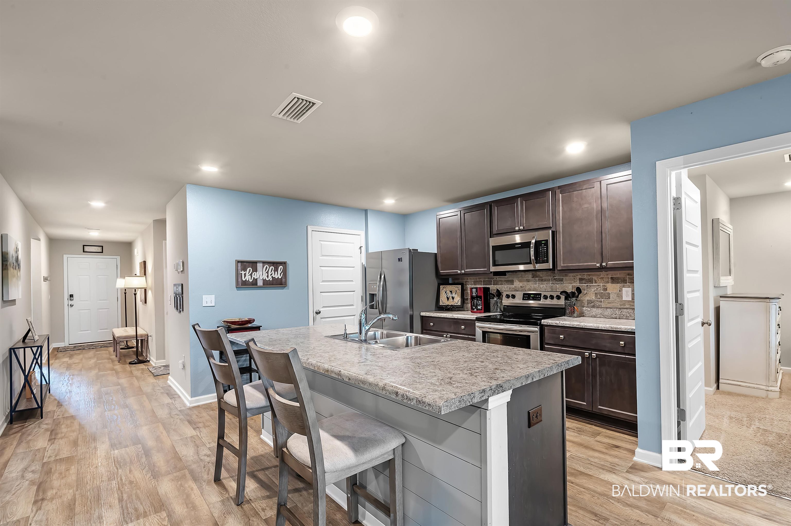17985 Lewis Smith Drive Foley, AL 36535 - Photo 15 of 56 Kitchen with a kitchen island with sink, light hardwood / wood-style flooring, sink, decorative backsplash, and appliances with stainless steel finishes