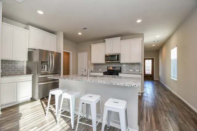 a kitchen with stainless steel appliances granite countertop a stove top oven a sink dishwasher and a refrigerator with wooden floor