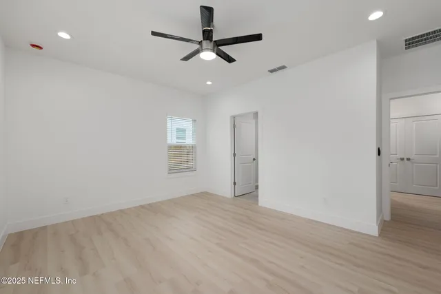 an empty room with wooden floor ceiling fan and windows