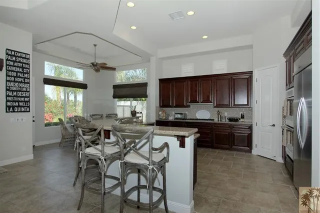 a kitchen with stainless steel appliances kitchen island granite countertop a refrigerator a stove a sink a dining table and chairs with wooden floor