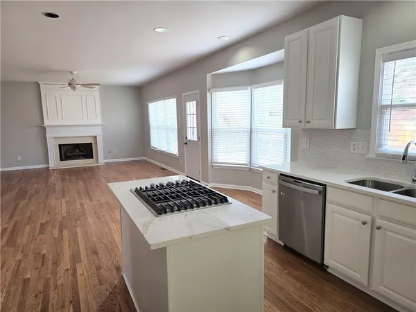 a kitchen with granite countertop a stove a sink dishwasher and white cabinets with wooden floor