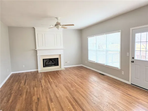 an empty room with wooden floor a ceiling fan white walls and windows