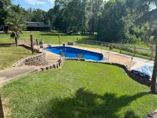 a view of a swimming pool with a yard and a large tree