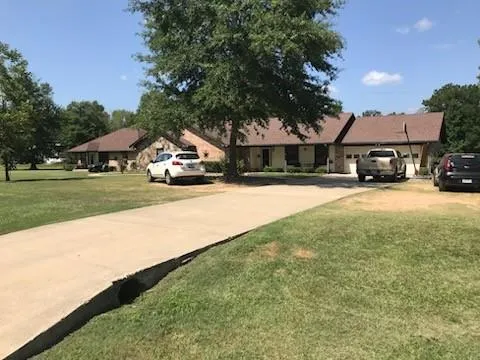 a car parked in front of a house next to a yard with big trees
