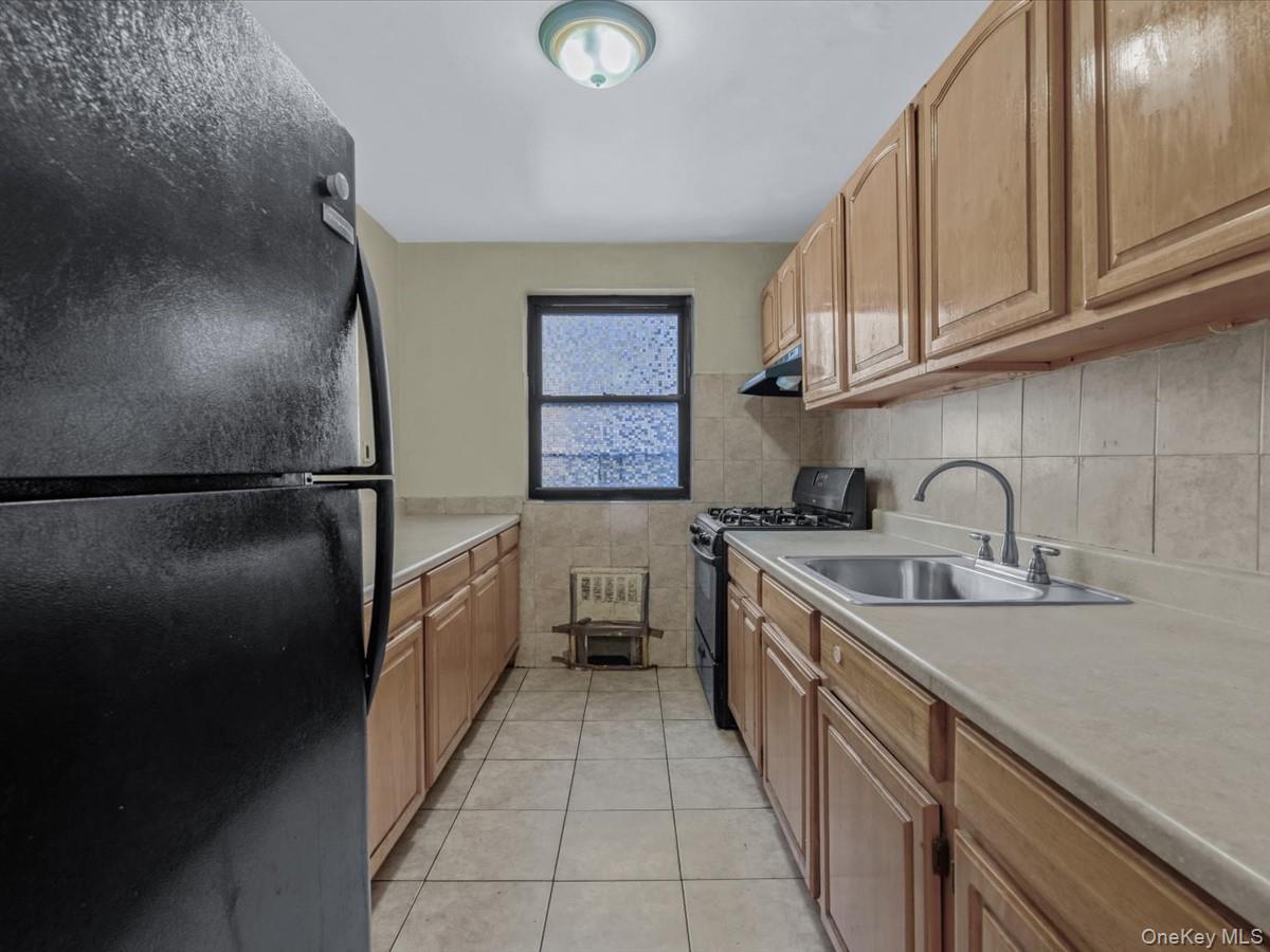44-05 Macnish Street, Unit 1B Queens, NY 11373 - Photo 4 of 13 Kitchen featuring black appliances, light countertops, light tile patterned floors, and brown cabinetry