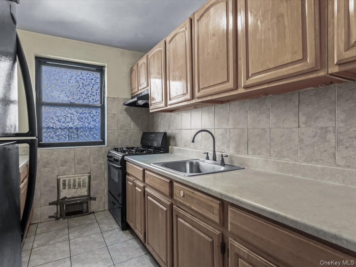44-05 Macnish Street, Unit 1B Queens, NY 11373 - Photo 5 of 13 Kitchen featuring black appliances, light countertops, light tile patterned flooring, under cabinet range hood, and tile walls