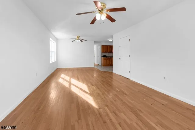 an empty room with wooden floor ceiling fan and windows