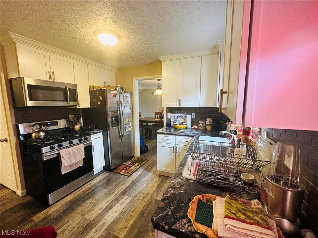 3894 Salisbury Road South Euclid, OH 44121 - Photo 8 of 16 Kitchen with appliances with stainless steel finishes, white cabinetry, a textured ceiling, dark countertops, hardwood floors, and backsplash