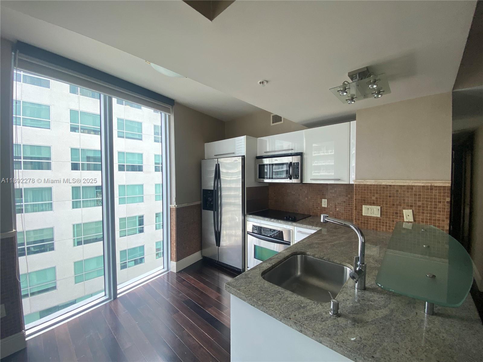 185 Southwest 7th Street, Unit 2312 Miami, FL 33130 - Photo 5 of 32 a kitchen with kitchen island a counter top space a sink and appliances