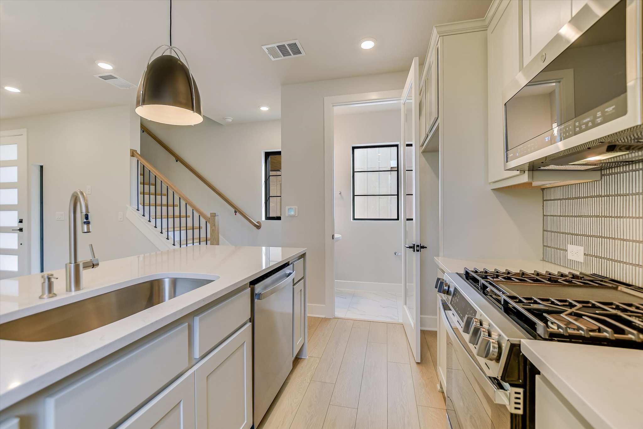 114 Lightsey Road, Unit 2 Austin, TX 78704 - Photo 7 of 14 Kitchen with appliances with stainless steel finishes, decorative light fixtures, light stone counters, white cabinets, and backsplash