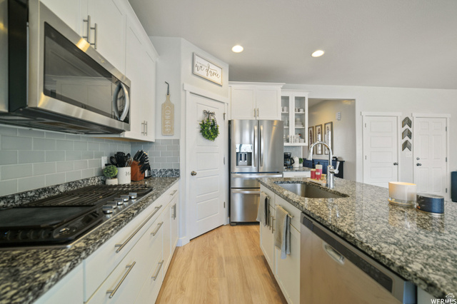 1836 Red Oak Road Eagle Mountain, UT 84005 - Photo 9 of 15 Kitchen featuring stainless steel appliances, light wood-style floors, white cabinetry, glass insert cabinets, and dark stone countertops