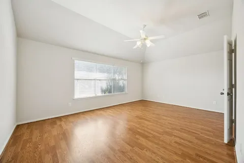 an empty room with wooden floor chandelier fan and windows