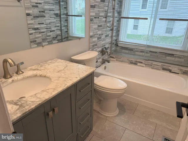 a bathroom with a granite countertop bathtub shower sink vanity and toilet