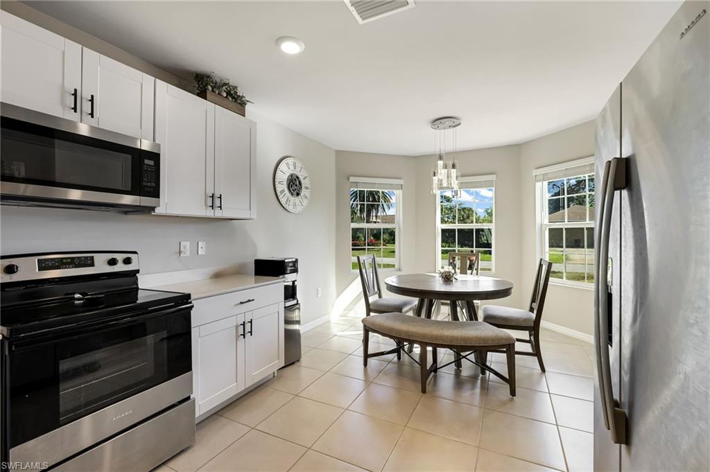 Kitchen with appliances with stainless steel finishes, light tile patterned floors, an inviting chandelier, white cabinets, and hanging light fixtures