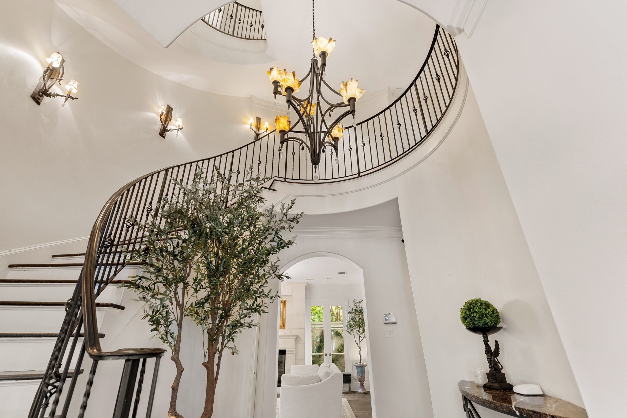 30 Hackberry Lane, Unit A Houston, TX 77027 - Photo 40 of 42 An elegant, sweeping staircase ascends to the third floor, defined by graceful curves, hardwood treads, and an intricate wrought-iron railing. The dramatic vertical space is accented by wall sconces and a sculptural multi-arm chandelier.
