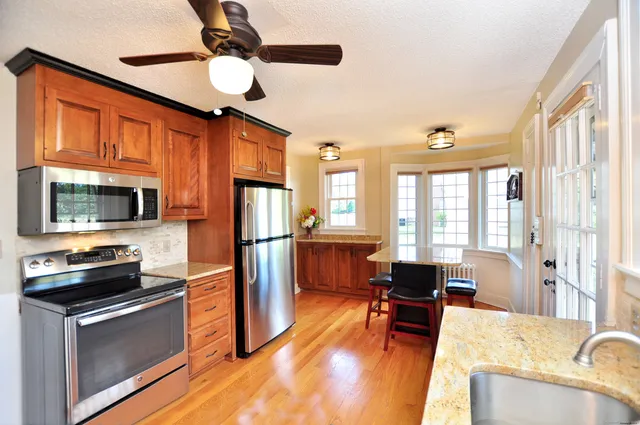 a kitchen with stainless steel appliances granite countertop a refrigerator oven stove a sink dishwasher a dining table and chairs with wooden floor