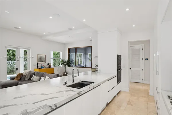 a large white kitchen with stainless steel appliances kitchen island granite countertop a large sink and living room view