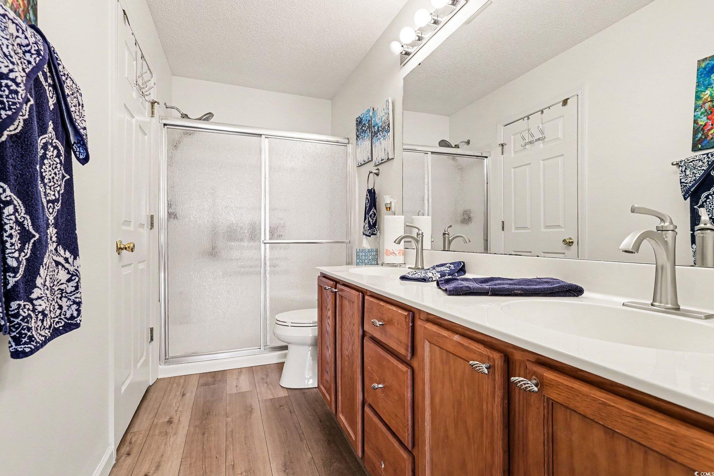 844 Sheridan Road, Unit 844 Myrtle Beach, SC 29579 - Photo 4 of 24 Bathroom featuring double vanity, dark wood-style floors, a stall shower, and a textured ceiling