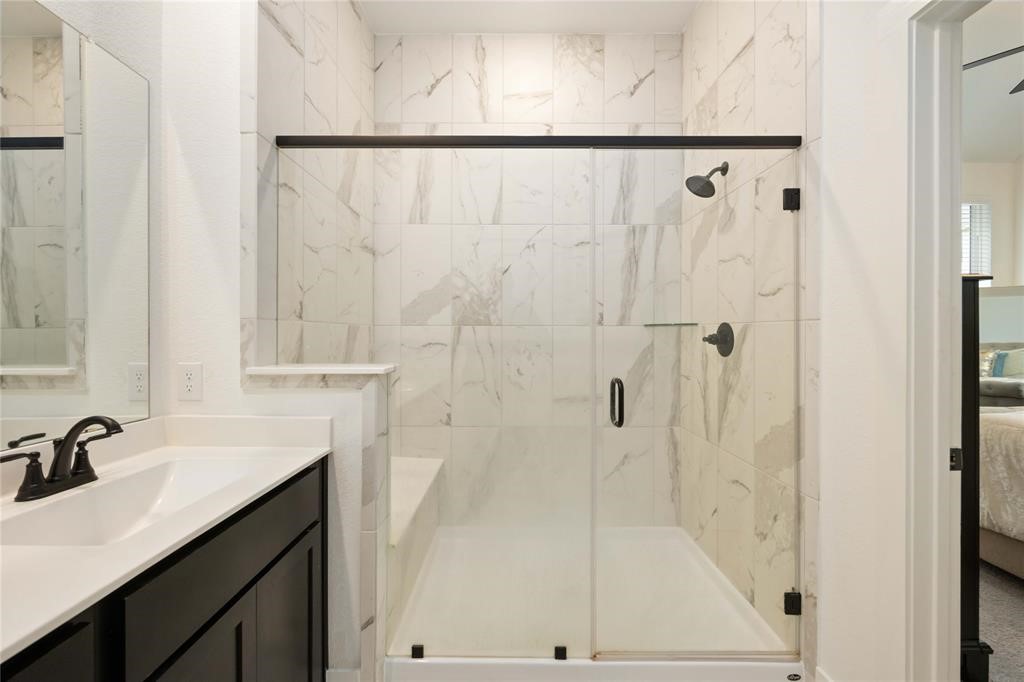 10014 Nectar Path Iowa Colony, TX 77583 - Photo 22 of 26 Modern bathroom featuring a spacious glass-enclosed shower with elegant marble tile, a sleek vanity with a black faucet, and an adjacent bedroom.