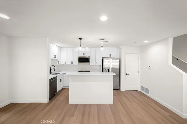 a kitchen with stainless steel appliances a sink a stove a refrigerator cabinets and a wooden floor